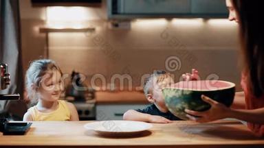 哥哥姐姐坐在桌子旁，妈妈带着西瓜放到桌子上.. 男孩和女孩碰水果。